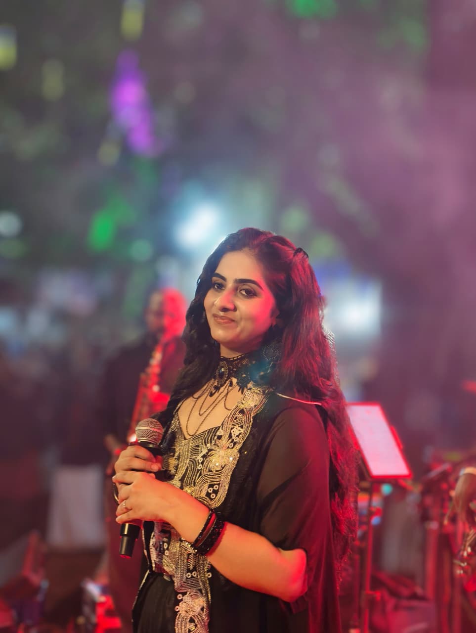Sarvasri Sukesh performing live on stage with a microphone under colourful stage lights
