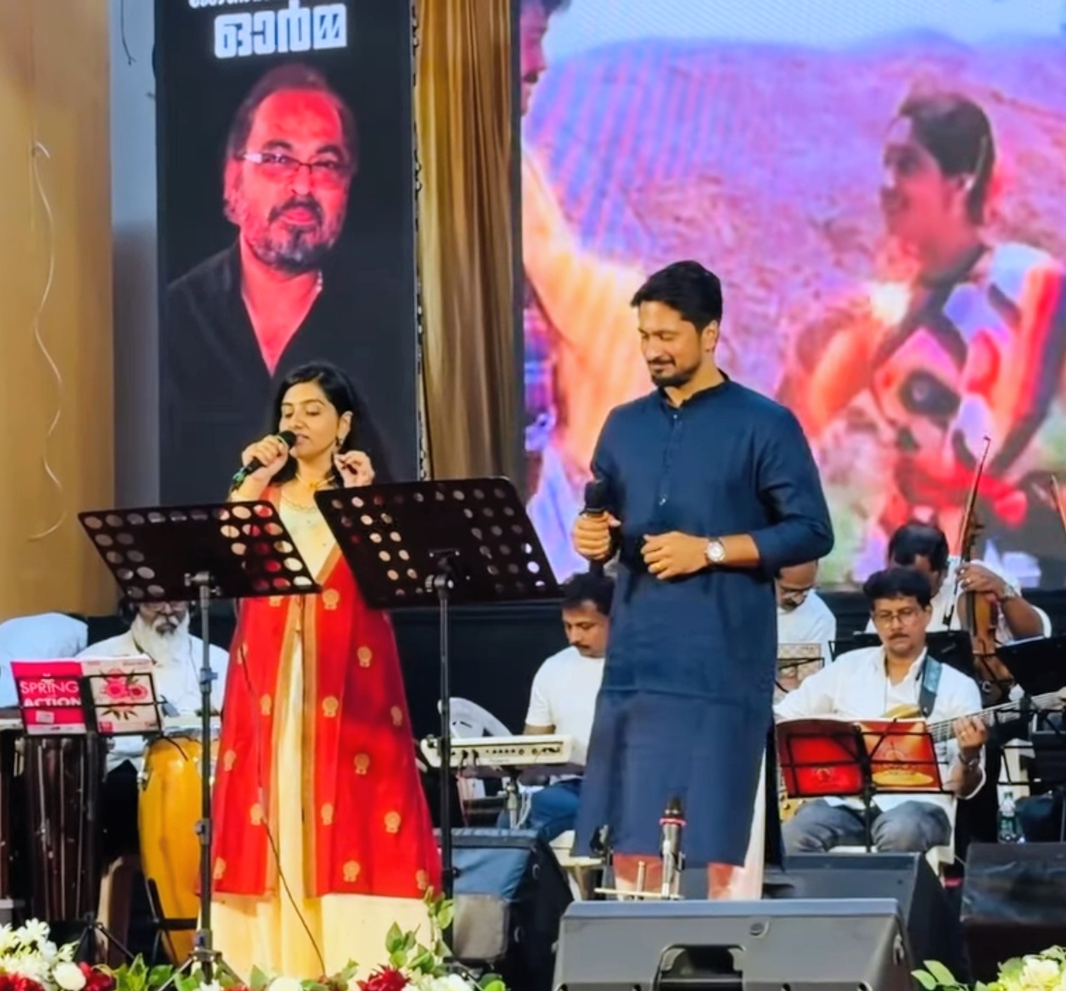 Sarvasri Sukesh singing on stage with a co-artist and orchestra