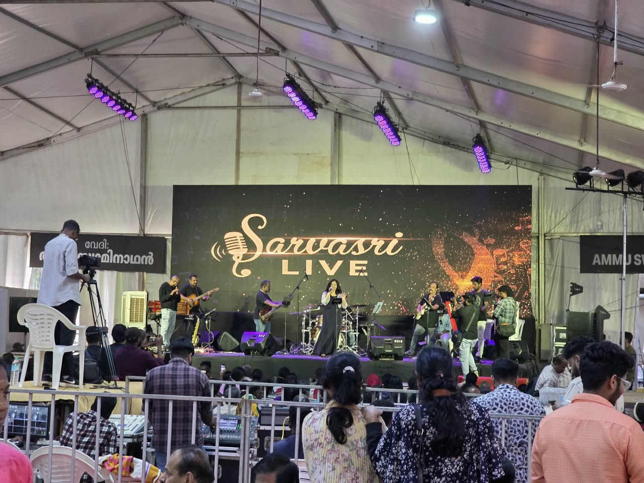 Sarvasri Live band performing on stage with the logo screen